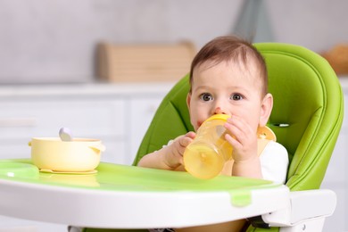 Photo of Cute little baby with bottle on feeding chair indoors. Space for text