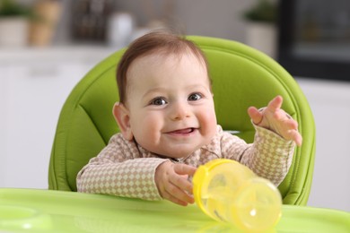Photo of Cute little baby with bottle on feeding chair indoors