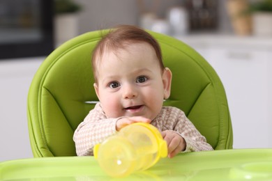 Photo of Cute little baby with bottle on feeding chair indoors
