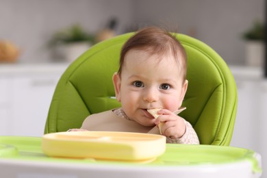 Photo of Cute little baby eating on feeding chair at home