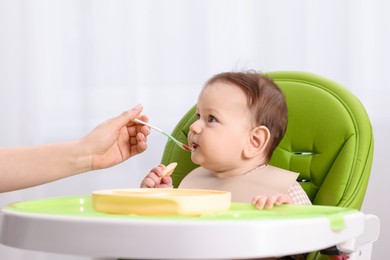 Photo of Mother feeding her baby on chair at home, closeup