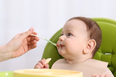 Photo of Mother feeding her baby on chair at home, closeup