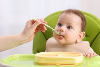 Photo of Mother feeding her baby on chair at home, closeup