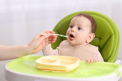 Photo of Mother feeding her baby on chair at home, closeup