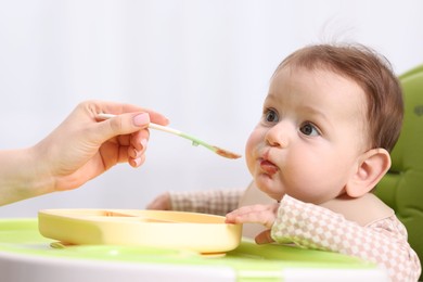 Photo of Mother feeding her baby on chair at home, closeup
