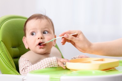 Photo of Mother feeding her baby on chair at home, closeup