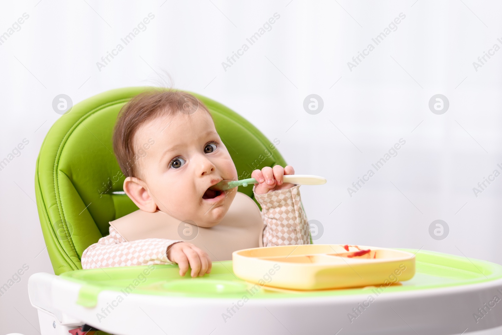 Cute little baby eating on feeding chair at home. Space for text Photo of Cute little baby eating on feeding chair at home. Space for text