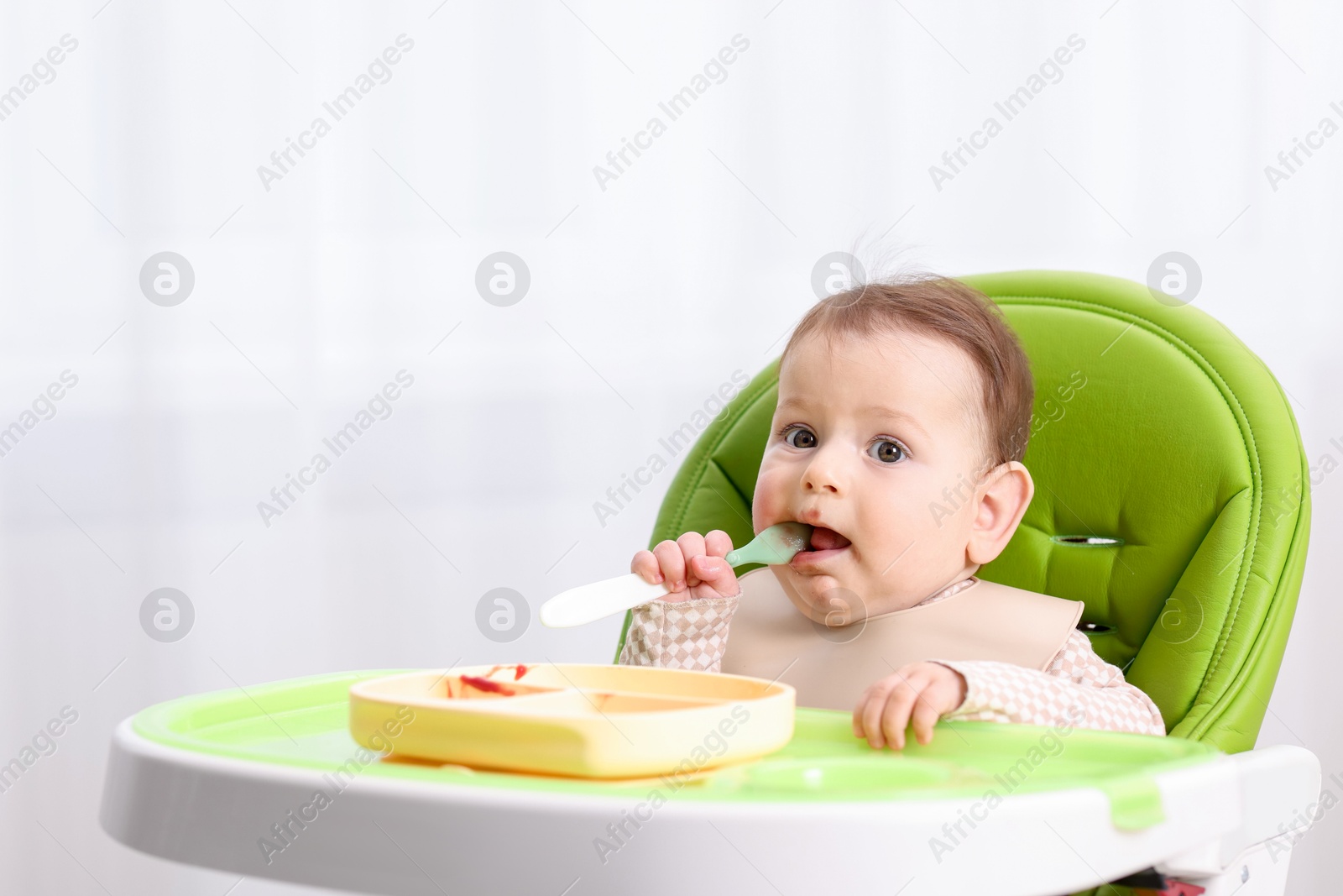 Cute little baby eating on feeding chair at home. Space for text Photo of Cute little baby eating on feeding chair at home. Space for text