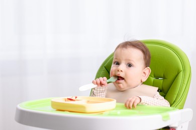 Photo of Cute little baby eating on feeding chair at home. Space for text