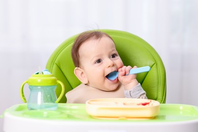 Photo of Cute little baby eating on feeding chair at home