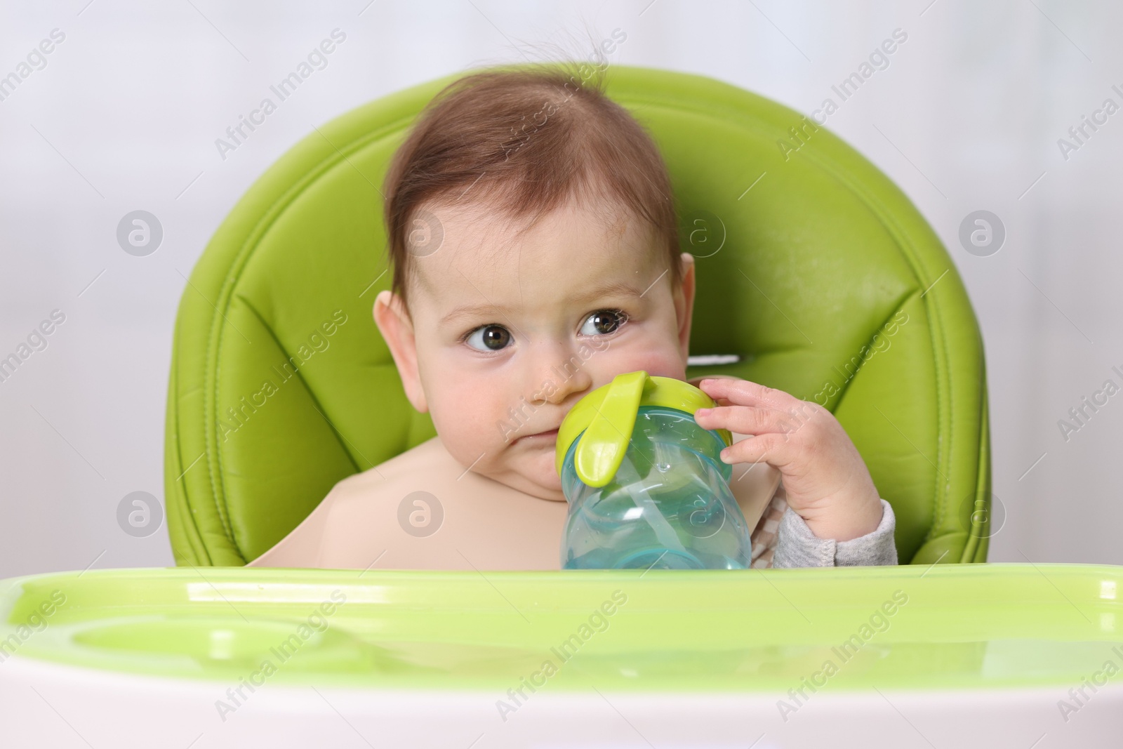 Cute little baby with bottle on feeding chair indoors Photo of Cute little baby with bottle on feeding chair indoors