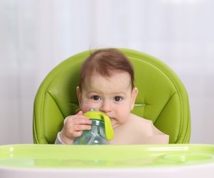 Photo of Cute little baby with bottle on feeding chair indoors