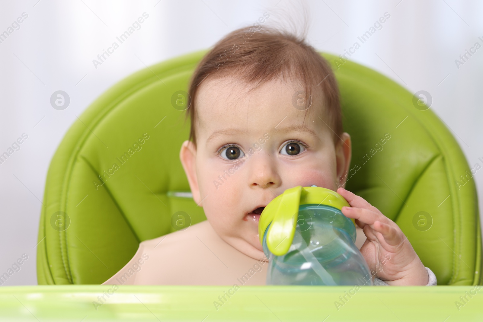 Cute little baby with bottle on feeding chair indoors Photo of Cute little baby with bottle on feeding chair indoors