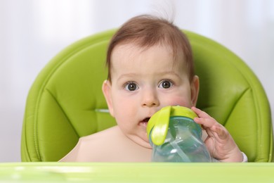 Photo of Cute little baby with bottle on feeding chair indoors