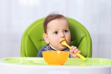 Photo of Cute little baby eating on feeding chair at home