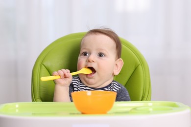 Photo of Cute little baby eating on feeding chair at home