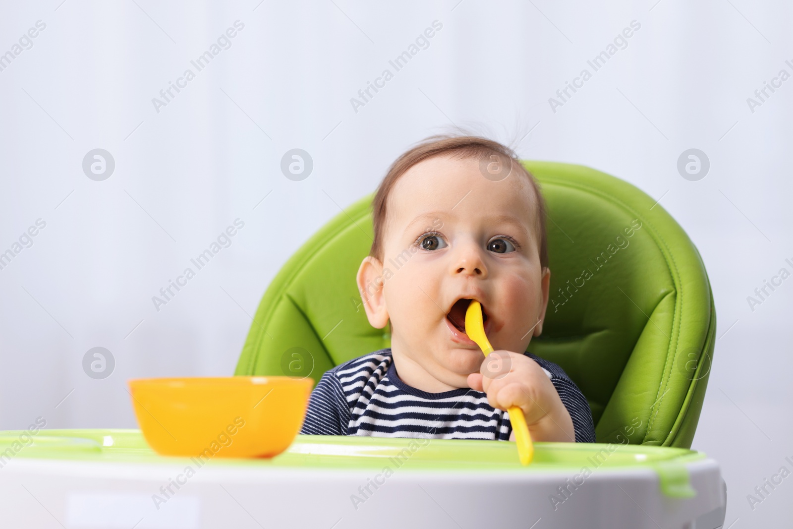 Cute little baby eating on feeding chair at home. Space for text Photo of Cute little baby eating on feeding chair at home. Space for text