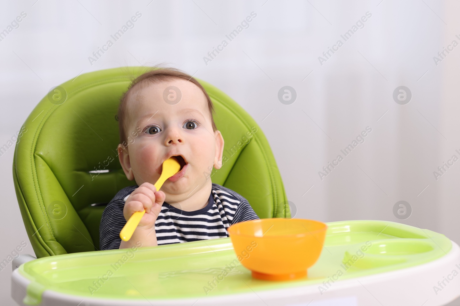 Cute little baby eating on feeding chair at home. Space for text Photo of Cute little baby eating on feeding chair at home. Space for text