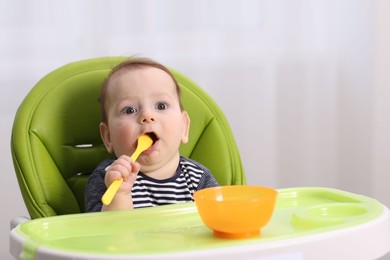 Photo of Cute little baby eating on feeding chair at home. Space for text
