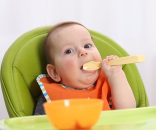 Photo of Cute little baby eating on feeding chair at home
