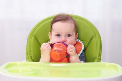 Photo of Cute little baby with bottle on feeding chair indoors