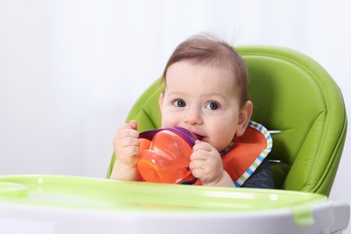 Photo of Cute little baby with bottle on feeding chair indoors. Space for text
