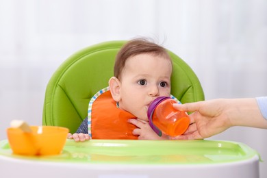 Photo of Mother giving bottle to her baby on feeding chair at home, closeup