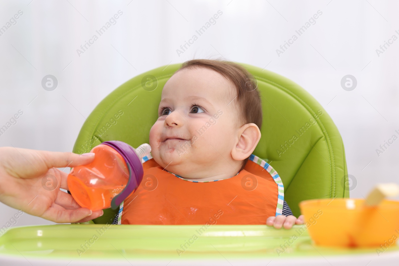 Mother giving bottle to her baby on feeding chair at home, closeup Photo of Mother giving bottle to her baby on feeding chair at home, closeup