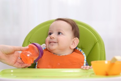 Photo of Mother giving bottle to her baby on feeding chair at home, closeup