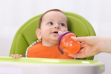Photo of Mother giving bottle to her baby on feeding chair at home, closeup