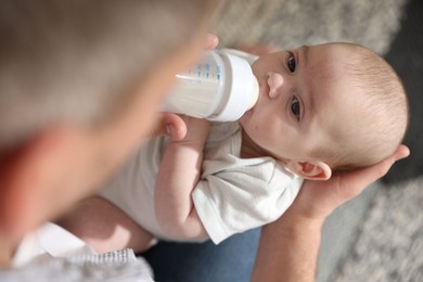 Photo of Father feeding his little baby with bottle at home, closeup