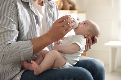 Photo of Father feeding his little baby with bottle on sofa at home, closeup