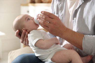 Photo of Father feeding his little baby with bottle on sofa at home, closeup