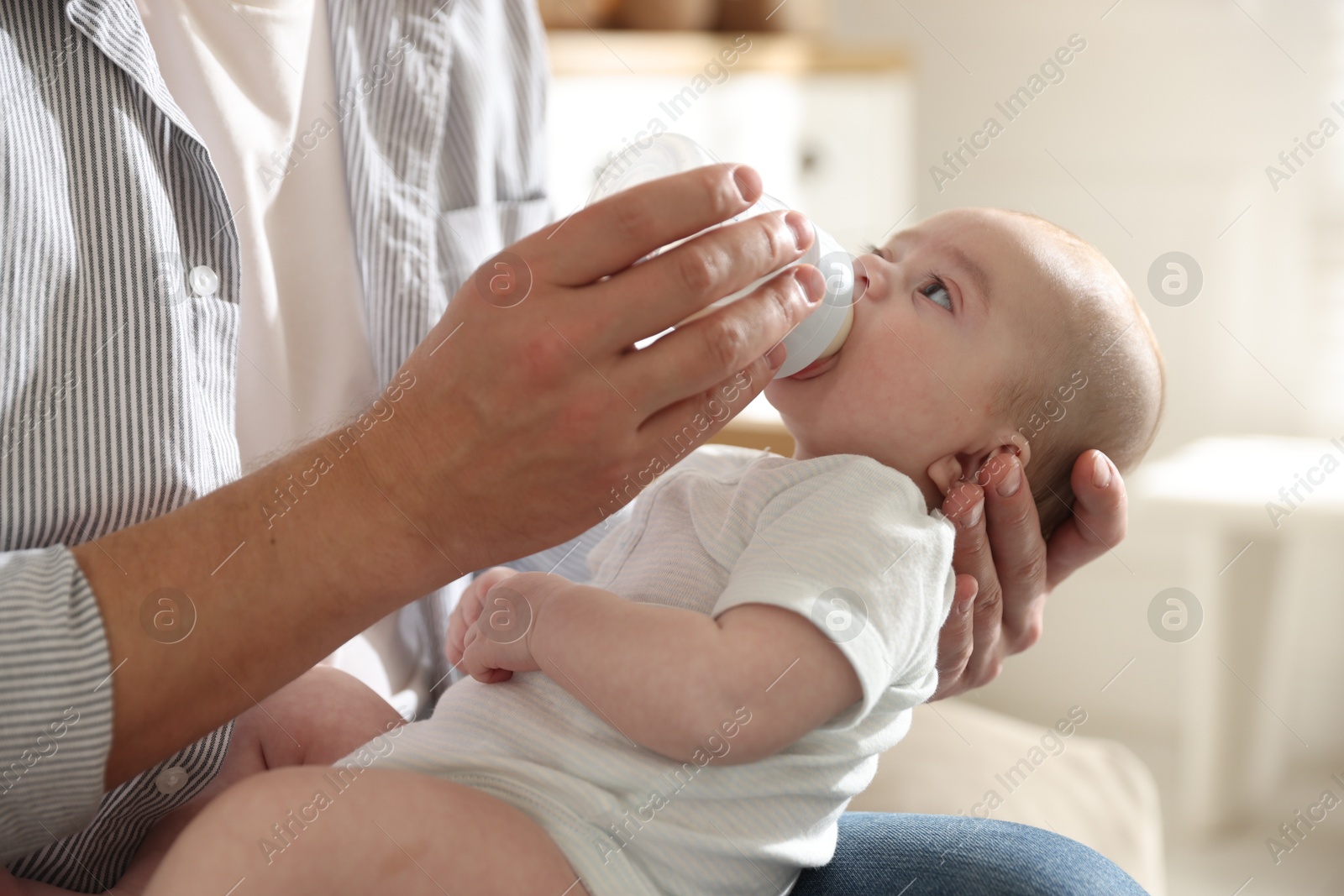 Father feeding his little baby with bottle on sofa at home, closeup Photo of Father feeding his little baby with bottle on sofa at home, closeup