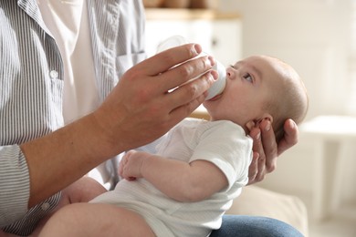 Photo of Father feeding his little baby with bottle on sofa at home, closeup