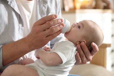Photo of Father feeding his little baby with bottle on sofa at home, closeup