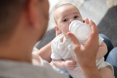 Photo of Father feeding his little baby with bottle at home, closeup