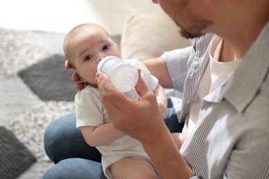 Photo of Father feeding his little baby with bottle on sofa at home, closeup