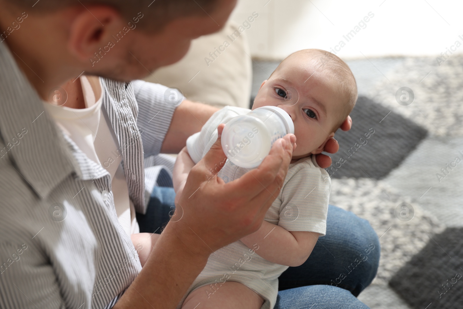 Father feeding his little baby with bottle on sofa at home, closeup Photo of Father feeding his little baby with bottle on sofa at home, closeup