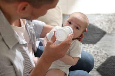 Photo of Father feeding his little baby with bottle on sofa at home, closeup