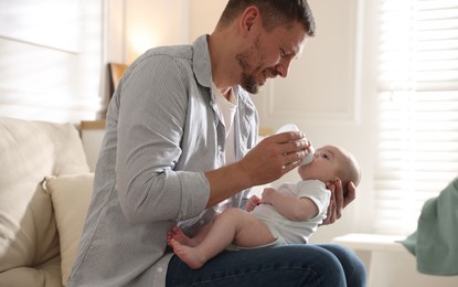 Photo of Father feeding his little baby with bottle on sofa at home