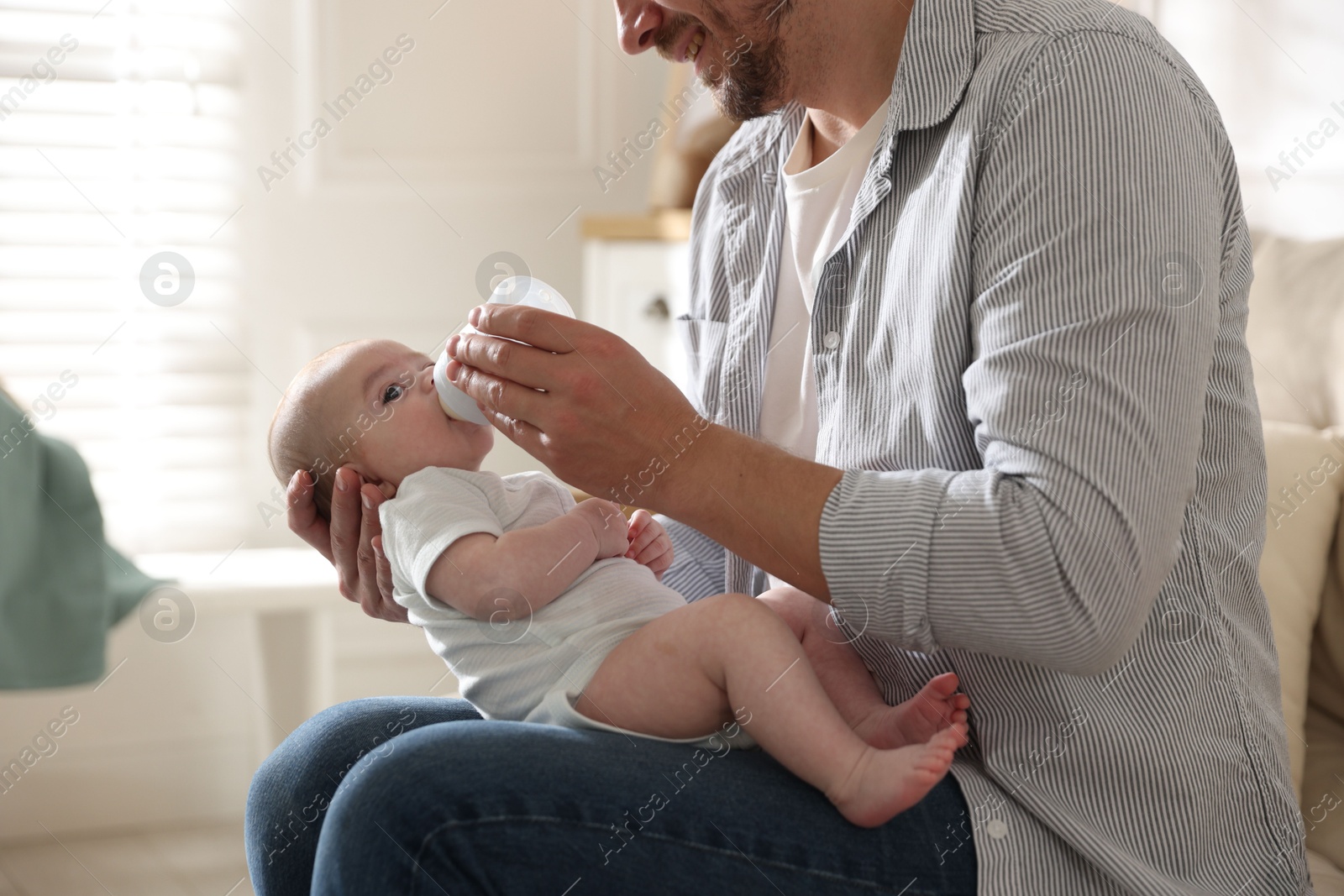 Father feeding his little baby with bottle on sofa at home, closeup Photo of Father feeding his little baby with bottle on sofa at home, closeup