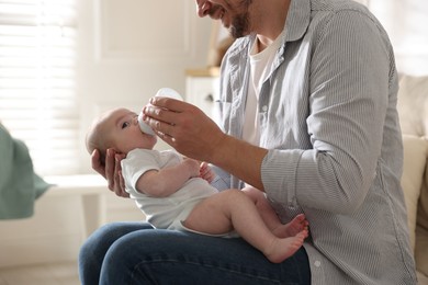Photo of Father feeding his little baby with bottle on sofa at home, closeup