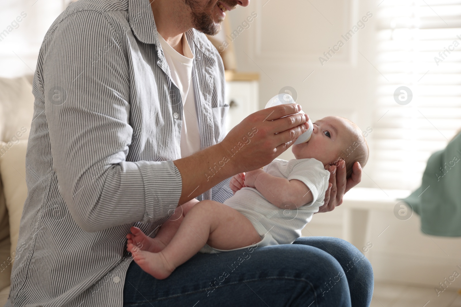 Father feeding his little baby with bottle on sofa at home, closeup Photo of Father feeding his little baby with bottle on sofa at home, closeup