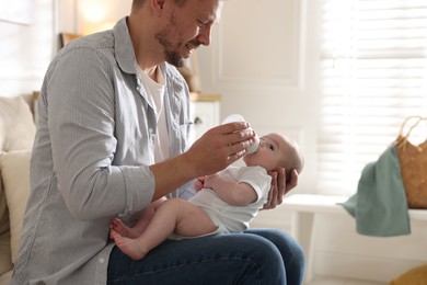 Photo of Father feeding his little baby with bottle on sofa at home, closeup