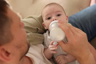 Photo of Father feeding his little baby with bottle on sofa at home, closeup