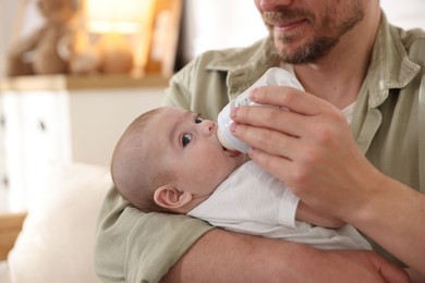 Photo of Father feeding his little baby with bottle on sofa at home, closeup