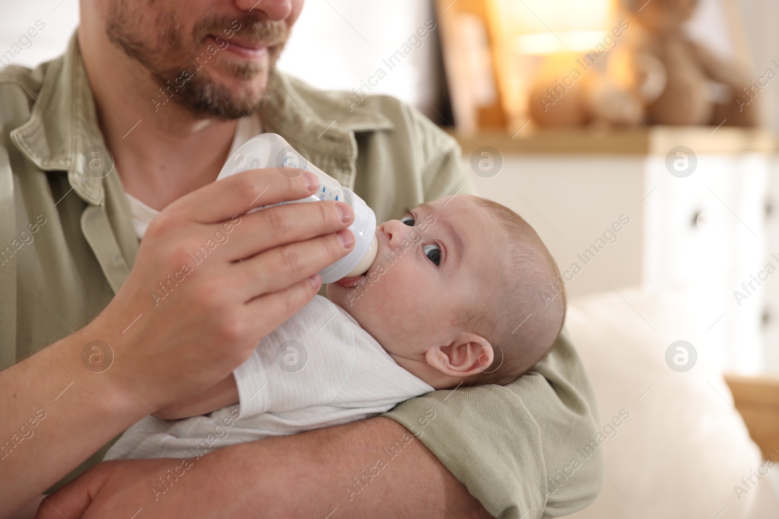 Father feeding his little baby with bottle on sofa at home, closeup Photo of Father feeding his little baby with bottle on sofa at home, closeup