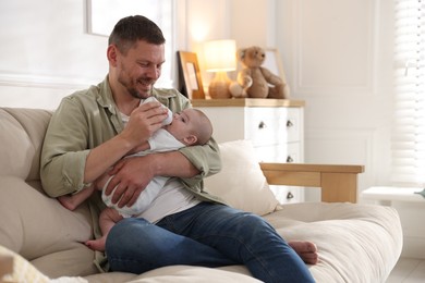 Photo of Father feeding his little baby with bottle on sofa at home. Space for text