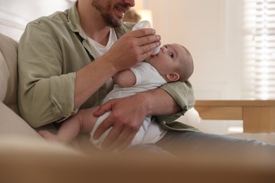 Photo of Father feeding his little baby with bottle on sofa at home, closeup